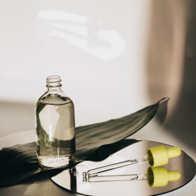 A Bottle with Oil and a Pipette Lying on a Mirror