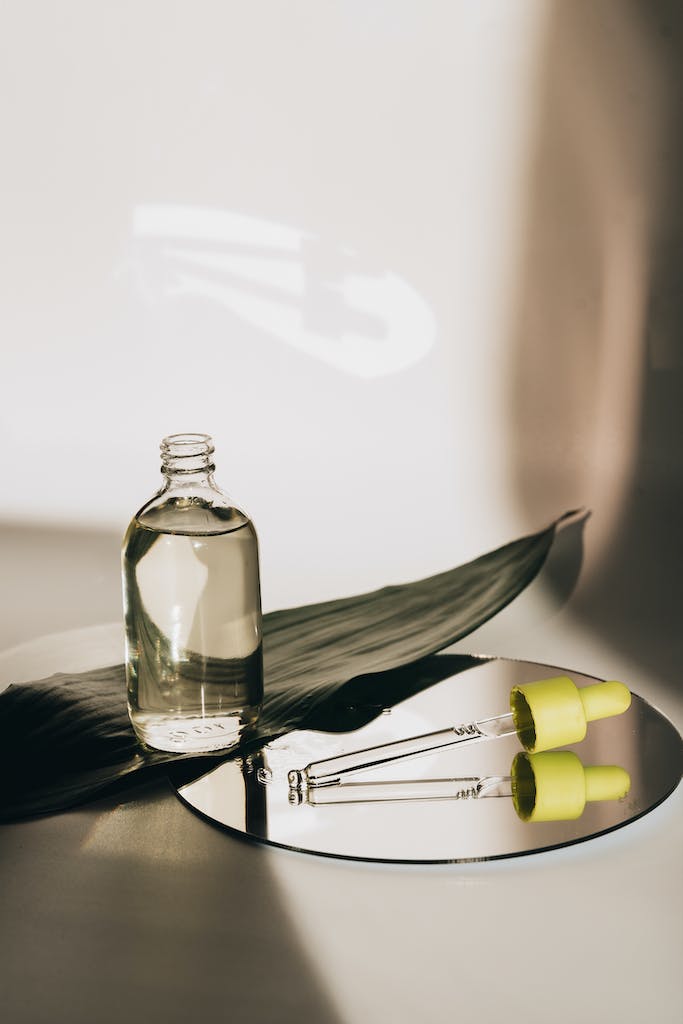 A Bottle with Oil and a Pipette Lying on a Mirror